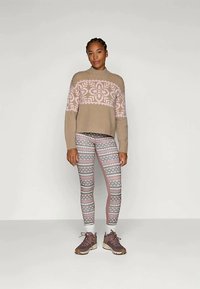 Maglione lavorato a maglia beige con motivi geometrici rosa, abbinato a leggins stampati in rosa e grigio, e scarpe da ginnastica marroni.