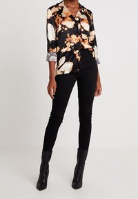 Svart och orange satin skjorta med abstrakt mönster, krage, trekvarts ärmar och grå manschetter, kombinerad med svarta skinny jeans och ankelstövlar.