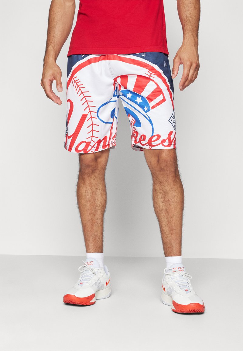 Pantalones cortos blancos con diseños gráficos en rojo y azul, que incluyen costuras de béisbol y texto "Yankees", combinados con zapatillas blancas y naranjas.