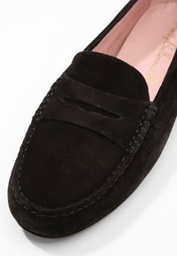 Schwarze Wildleder Slipper mit einem genähten Mokassin-Design, ausgestattet mit einer eingeschnittenen Vorderseite und einem weichen, pinken Innenfutter.