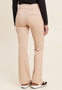 Pantaloni beige a zampa d'elefante con una texture liscia, due tasche posteriori e dettagli di cucitura in contrasto. Abbinati a sneakers nere con stampa animale.