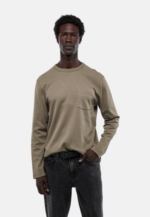 Chemise en coton vert olive à manches longues avec un col rond et une poche poitrine, associée à un jean en denim gris et une ceinture noire.