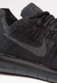 Baskets Nike Free noires avec tige en tissu texturé, lacets fins et un logo swoosh noir emblématique. Dotées d'une semelle noire coussinée.