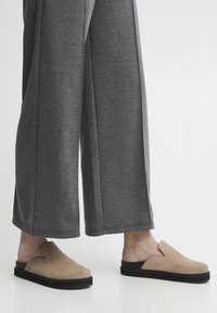 Bež semiš nasadne čevlje z črnim podplatov, z angularno izrezanim dizajnom. V kombinaciji s sivimi širokimi hlačami.