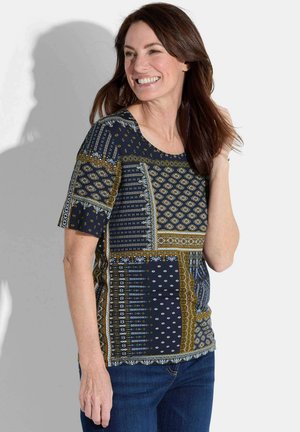 Haut à motifs marins avec divers designs géométriques en or et blanc, aux manches courtes et un col arrondi, associé à un jean bleu.