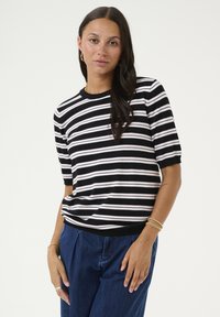 Haut à manches courtes noir et blanc à rayures, avec un col rond, associé à un pantalon en denim ample. Motif de rayures horizontales notable.