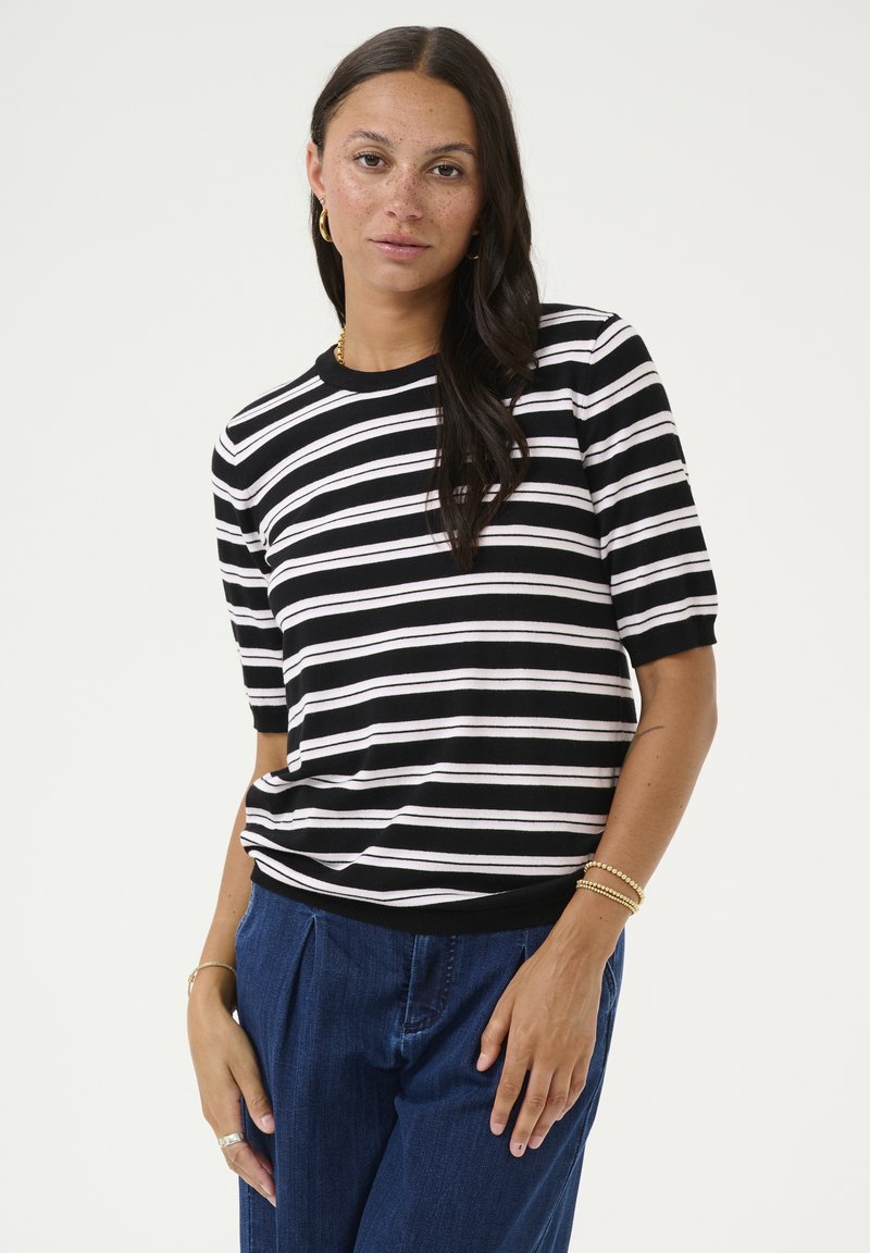 Haut à manches courtes noir et blanc à rayures, avec un col rond, associé à un pantalon en denim ample. Motif de rayures horizontales notable.
