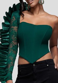 Vihreä kokopuku, jossa on yksi pitsihihainen ja röyhelöinen olkapääyksityiskohta. Sileä kangas, jäsennelty yläosa, yhdistetty mustiin korkeavyötäröisiin housuihin.