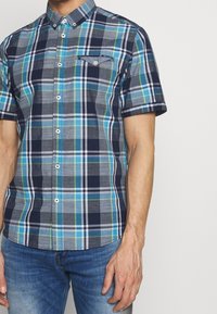 Kortärmad rutig skjorta i nyanser av marinblått, grått och grönt med knappar och en bröstficka. Tyg i bomull med en slät struktur.