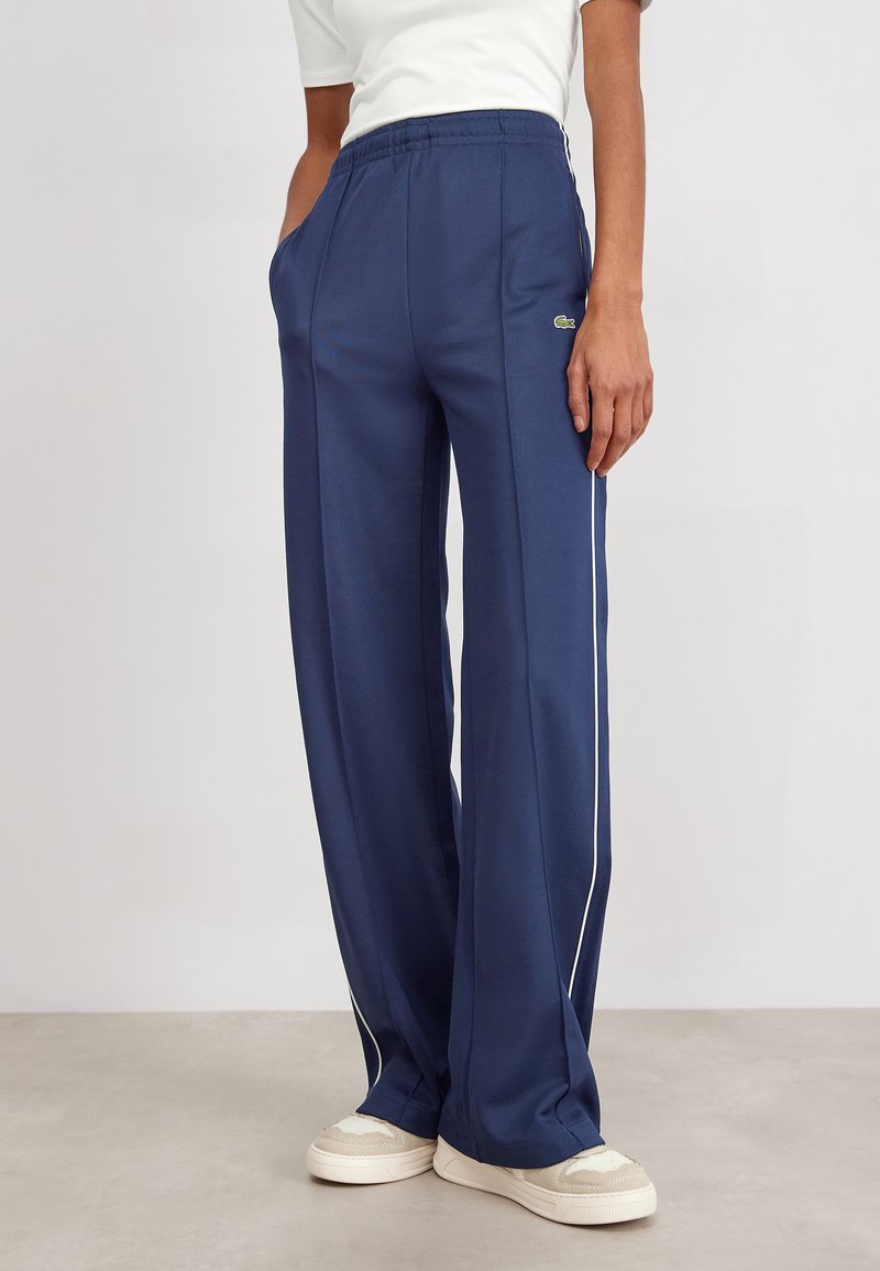 Navy wide-leg pants with white side stripes, elastic waistband, and pockets. Made from a smooth, lightweight material.