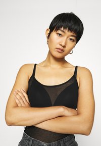 Must mustre vest, mille läbipaistva võrkmaterjaliga detailide ja õhukeste traksidega, sobib kokku kõrge vöökohaga teksapükstega.