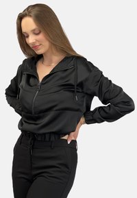 Czarna krótka kurtka z zamkiem z przodu, kapturem na sznurku i elastycznymi mankietami. Uzupełniona czarnymi dopasowanymi spodniami, o gładkiej fakturze.