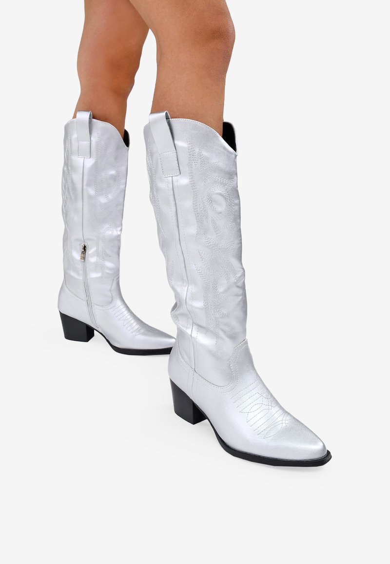 Botas de vaquero plateadas con punta afilada y tacón de bloque. Presentan un diseño grabado, cierre con cremallera y bucles en la parte superior.
