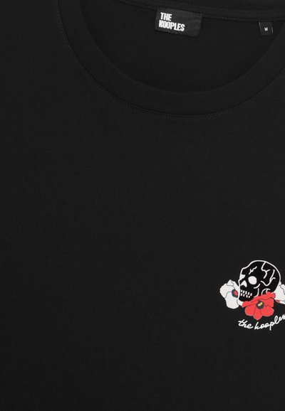 Camiseta de algodón negra con un pequeño diseño de calavera bordado con flores rojas y acentos blancos, cuello redondo y mangas cortas.