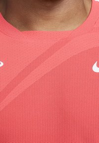 Camisa deportiva rosa con tejido texturizado, que presenta un cuello acanalado y rayas diagonales. Logo de Nike en blanco en el lado izquierdo.