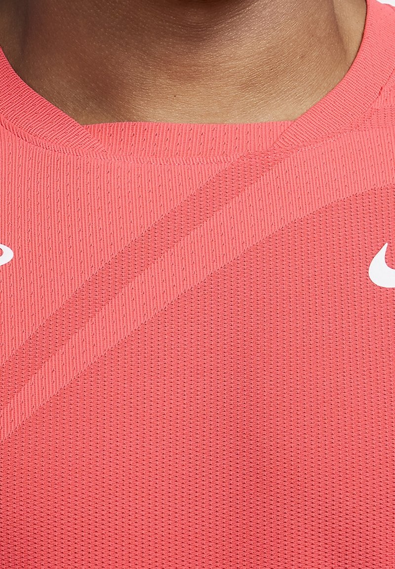 Camisa deportiva rosa con tejido texturizado, que presenta un cuello acanalado y rayas diagonales. Logo de Nike en blanco en el lado izquierdo.