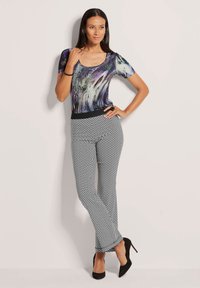 T-shirt met korte mouwen met een kleurrijk abstract patroon; gecombineerd met zwart-witte chevronpatroon broek; zwarte hoge hakken.