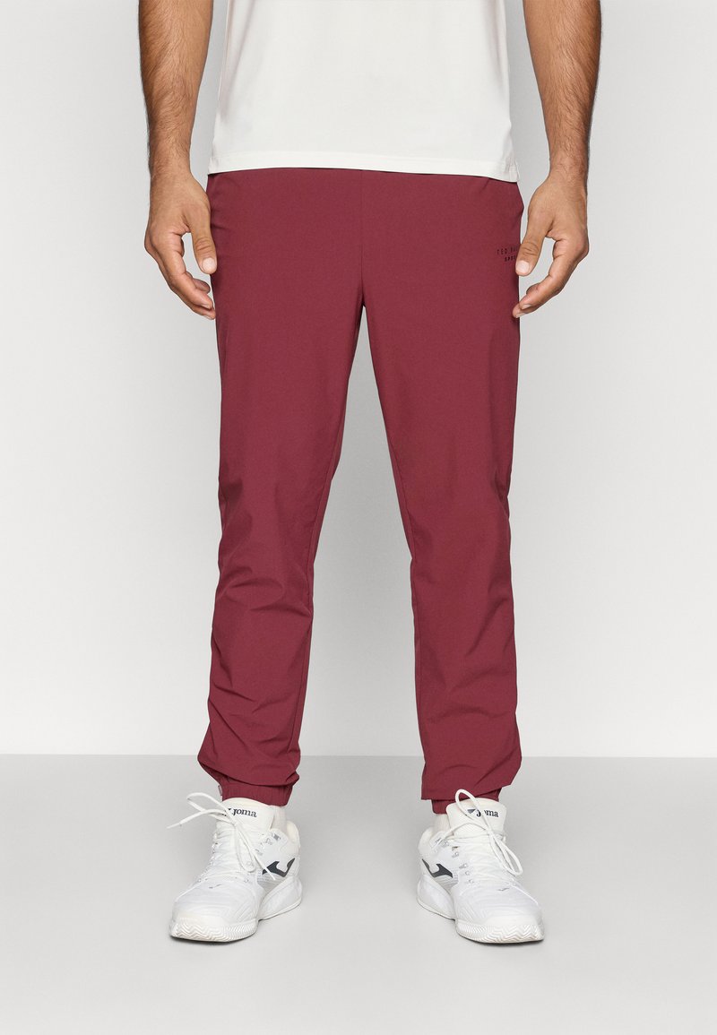 Bordo sporta bikses ar elastīgu jostasvietu, sašaurinātu piegriezumu un aprocēm, apvienotas ar baltām sporta kurpēm. Sānos ir logotipa detaļa.