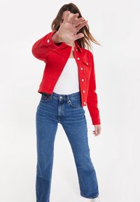 Veste en jean rouge avec fermetures à boutons, deux poches poitrine et manches longues, associée à un jean flare bleu en denim taille haute.