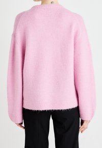 Pink cashmere sweater with a relaxed fit, ribbed neckline and cuffs, and a soft, fluffy texture. The hem is slightly longer in the back.