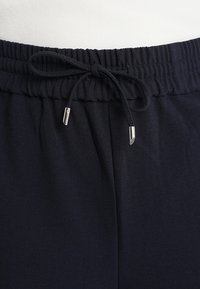 Pantalones de chándal azul marino con cintura elástica, cordón ajustable y puntas metálicas plateadas. Textura de tela suave y lisa.