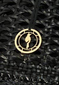 Czarna pleciona torba z teksturowanej skóry, złotym okrągłym znaczkiem marki z wzorem ptaka oraz wiszącym skórzanym paskiem.