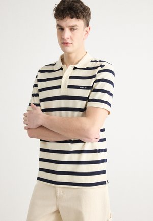 Striped polo shirt with cream and navy colors, short sleeves, collared neck, and small logo on the chest. Soft cotton material.