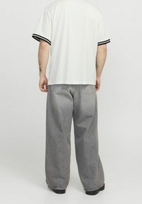 Bílá košile s krátkým rukávem a černými pruhovanými manžetami, v kombinaci s volnými světle šedými džíny. Tkanina vypadá hladce a ležérně.