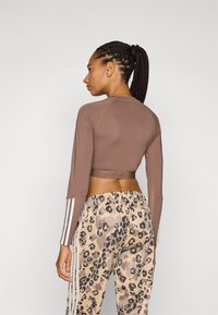Brunet avkortet langermet topp med rund hals, sammen med beige joggebukser med leopardmønster og hvite sidestiper. Teksturert stoff.