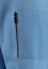 Pantaloni sportivi blu con una tasca con zip sul lato. Realizzati in un materiale morbido e liscio, con una texture leggera e traspirante.