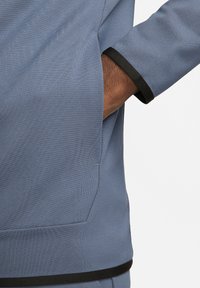 Light blue sweatshirt featuring a textured fabric, black accents on cuffs, and a side pocket for functionality.