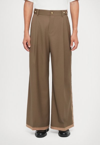 Brown wide-leg trousers made of smooth fabric, featuring a front pleat and gold button accents. The hem has a contrasting light beige trim.