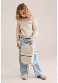 Beige sweatshirt med en färgglad blommig grafik. Ryggsäcken har en strukturerad krämfärgad front, blå sidor och rosa detaljer.