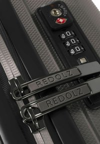 Acercamiento de una cremallera de maleta con dos tiradores de metal de la marca REDOLZ asegurados por un candado de combinación TSA007 configurado en 0-0-0.