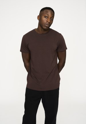 Brun crew-neck t-shirt lavet af bomuld, med korte ærmer og en afslappet pasform, parret med sorte bukser på en neutral baggrund.