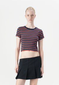 Crop top dengan garis horizontal merah, biru, dan navy, dengan leher bulat dan lengan pendek. Dipadukan dengan rok plisket hitam.