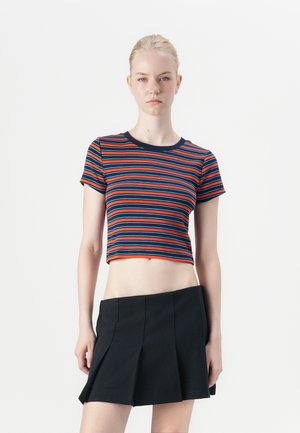 Top court avec des rayures horizontales rouges, bleues et navy, doté d'un col rond et de manches courtes. Associé à une jupe plissée noire.