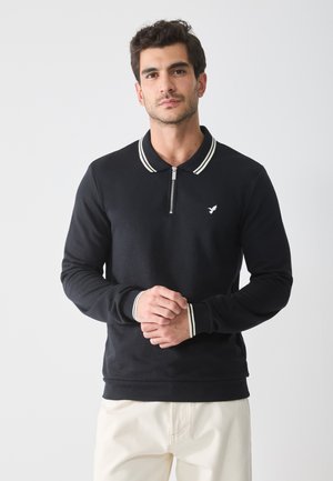 Black long-sleeve polo shirt with a zip collar, featuring white striped accents on the collar and cuffs. Small logo on the left chest.