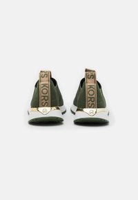 Baskets en mesh vert avec un accent doré au niveau du talon et une sangle beige avec le logo "KORS". Semelle blanche plate avec un motif de grip texturé.