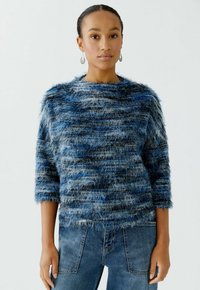 Blauer flauschiger Pullover mit rundem Ausschnitt, Dreiviertelärmeln und einem strukturierten Streifenmuster, kombiniert mit blauen Denim-Jeans.