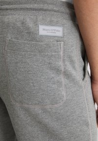 Szare spodnie dresowe wykonane z miękkiego materiału, z kieszenią naszywaną z tyłu oraz kontrastującym przeszyciem. Etykieta widoczna na pasku talii.