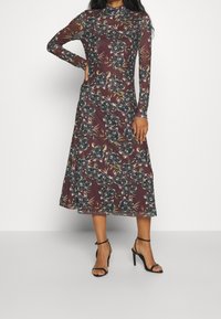 Robe midi à manches longues en bordeaux foncé avec imprimé floral. Fabriquée en tissu léger, elle possède un col haut et un bustier ajusté.