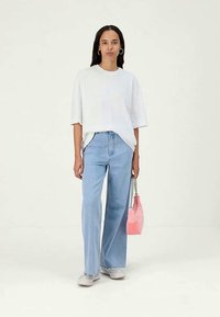 Fehér, oversize póló, világoskék, bőszárú farmernadrág, szürke cipő és egy kis rózsaszín táska láncos pánttal. Minimalista dizájn, laza stílus.