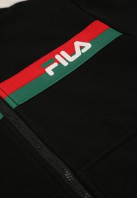 Felpa nera con zip caratterizzata da una striscia orizzontale rossa e verde con il logo "FILA" in bianco. Tessuto liscio con accenti tessili a contrasto.