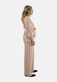 Lichtroze gebreid twee-delig outfit met een gebelt cardigan met ribbeltextuur en een wijde broek. Zwarte platte schoenen maken de look compleet.