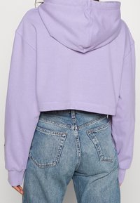 Felpa cropped con cappuccio con coulisse e polsini a costine, abbinata a jeans di denim blu a vita alta con tasche posteriori visibili.