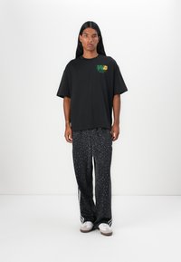 Svart oversized T-skjorte med grønn og oransje grafikk. Svart leopardmønstrede bukser med hvite striper. Brukt med hvite joggesko.