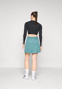 Fekete, hosszú ujjú crop top, amelyet egy türkiz sport szoknyával párosítottak, finom geometrikus mintákkal. Fehér zoknival és sportcipővel viselve.