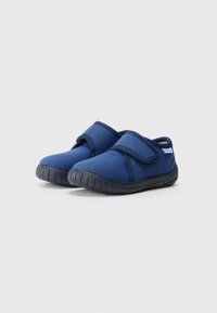 Zilās auduma slaidu kurpes ar teksturētu melnu gumijas zoli un Velcro siksnu. Dizains ir zemāks ar apaļu purngalu.