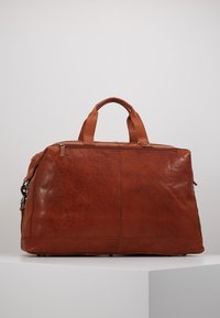 Sac de voyage en cuir dans un marron riche avec une finition texturée. Équipé de poignées supérieures doubles et d'une fermeture éclair pour un rangement sécurisé.